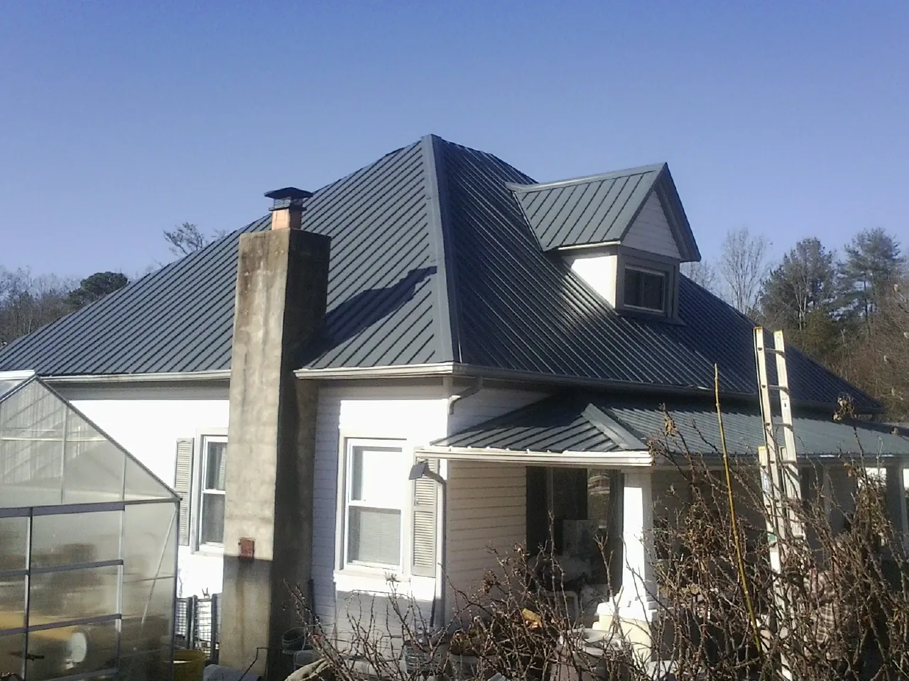 Dark blue standing seam metal roof on a white farmhouse with dormer — Slate & Tile Roof Repair by Roofing Brothers in Dibble
