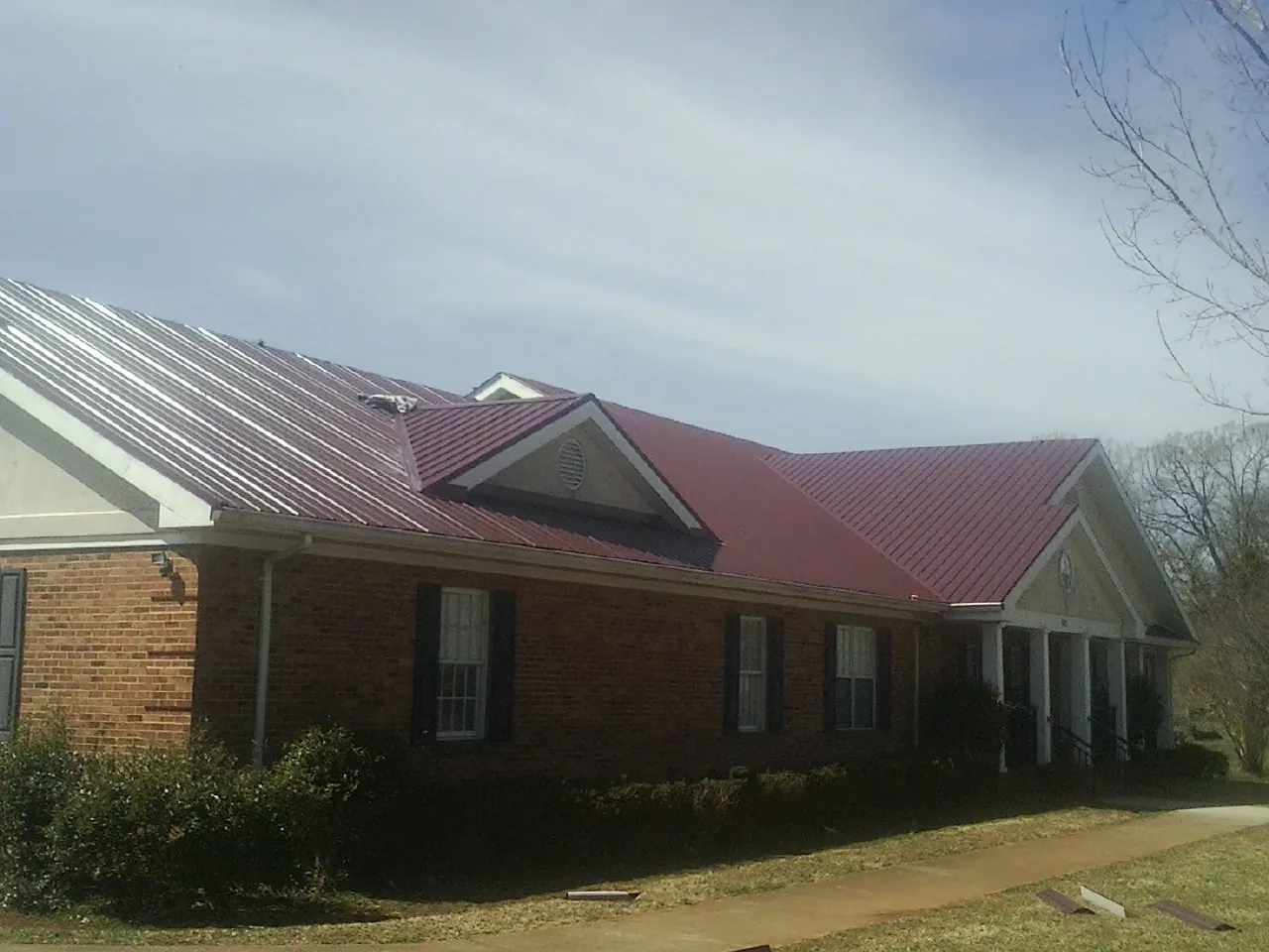 Red metal roof with gabled entries on a long brick building, from a Hail Damage Roof Repair job in Dibble
