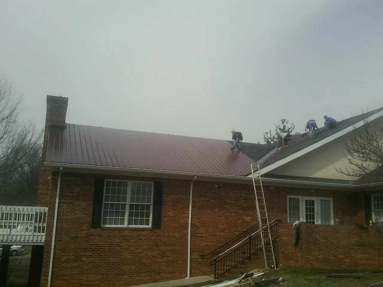 Crew setting red metal roofing panels on a brick home in Dibble
