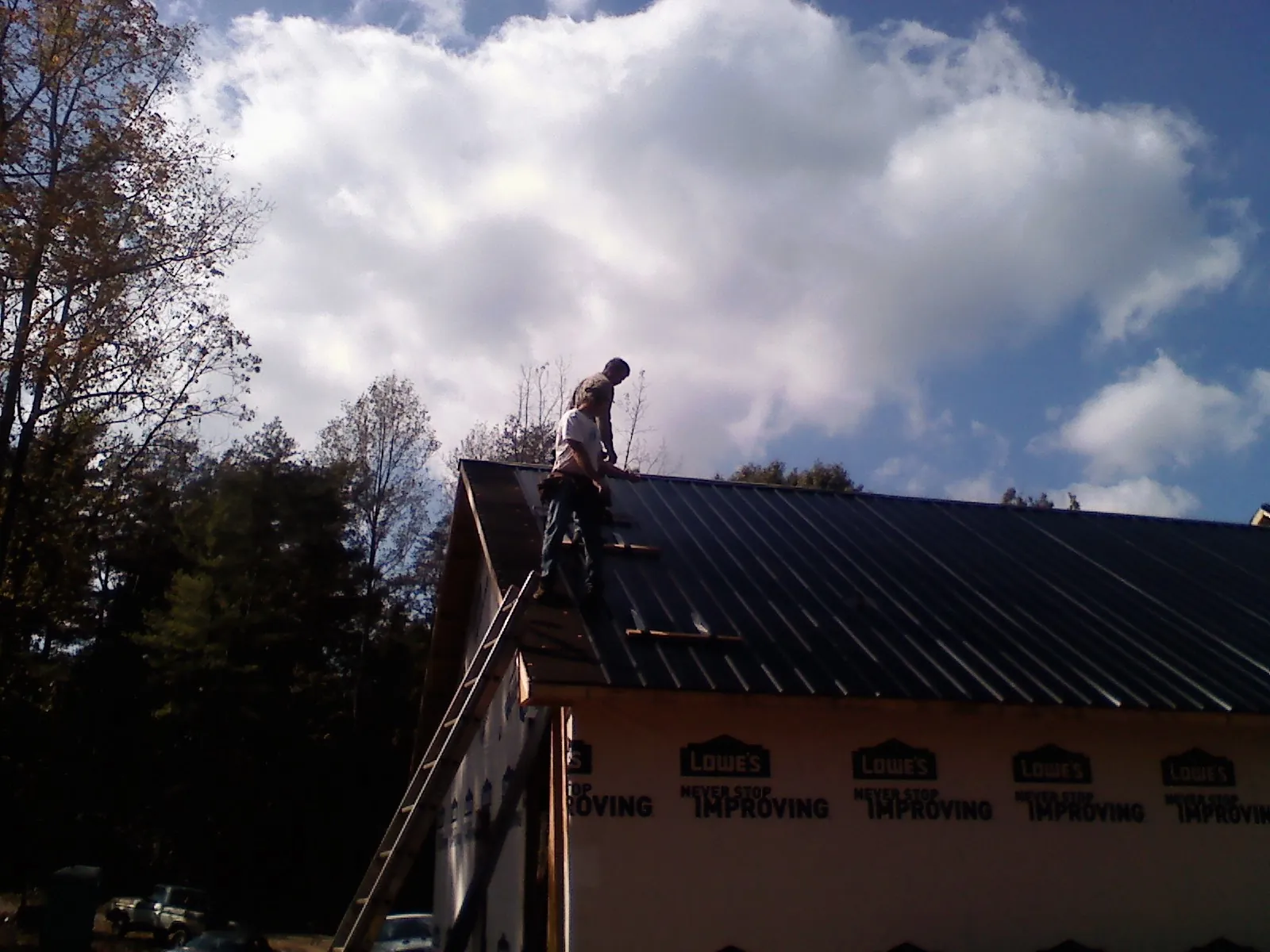 Roofer fastening dark metal panels high against a cloudy sky, from a Roof Inspection job in Dibble