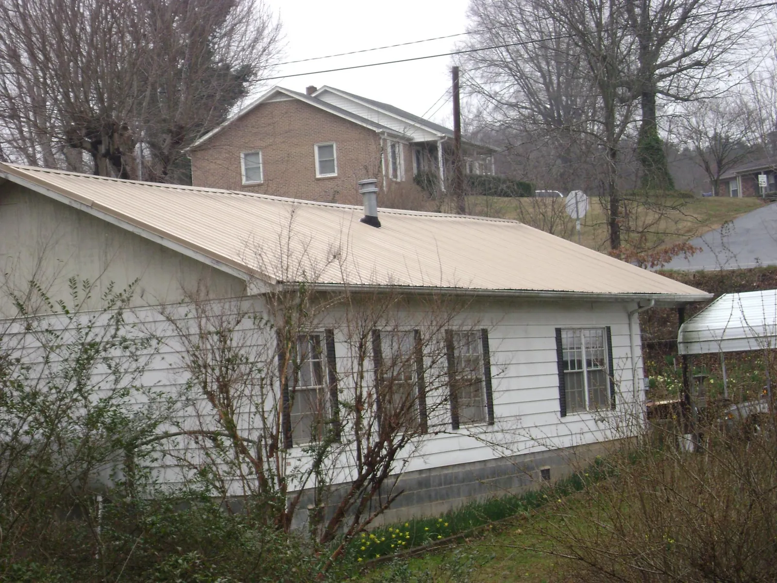 Tan metal roof on a white sided house set into a hillside — Commercial Roofing by Roofing Brothers in Dibble